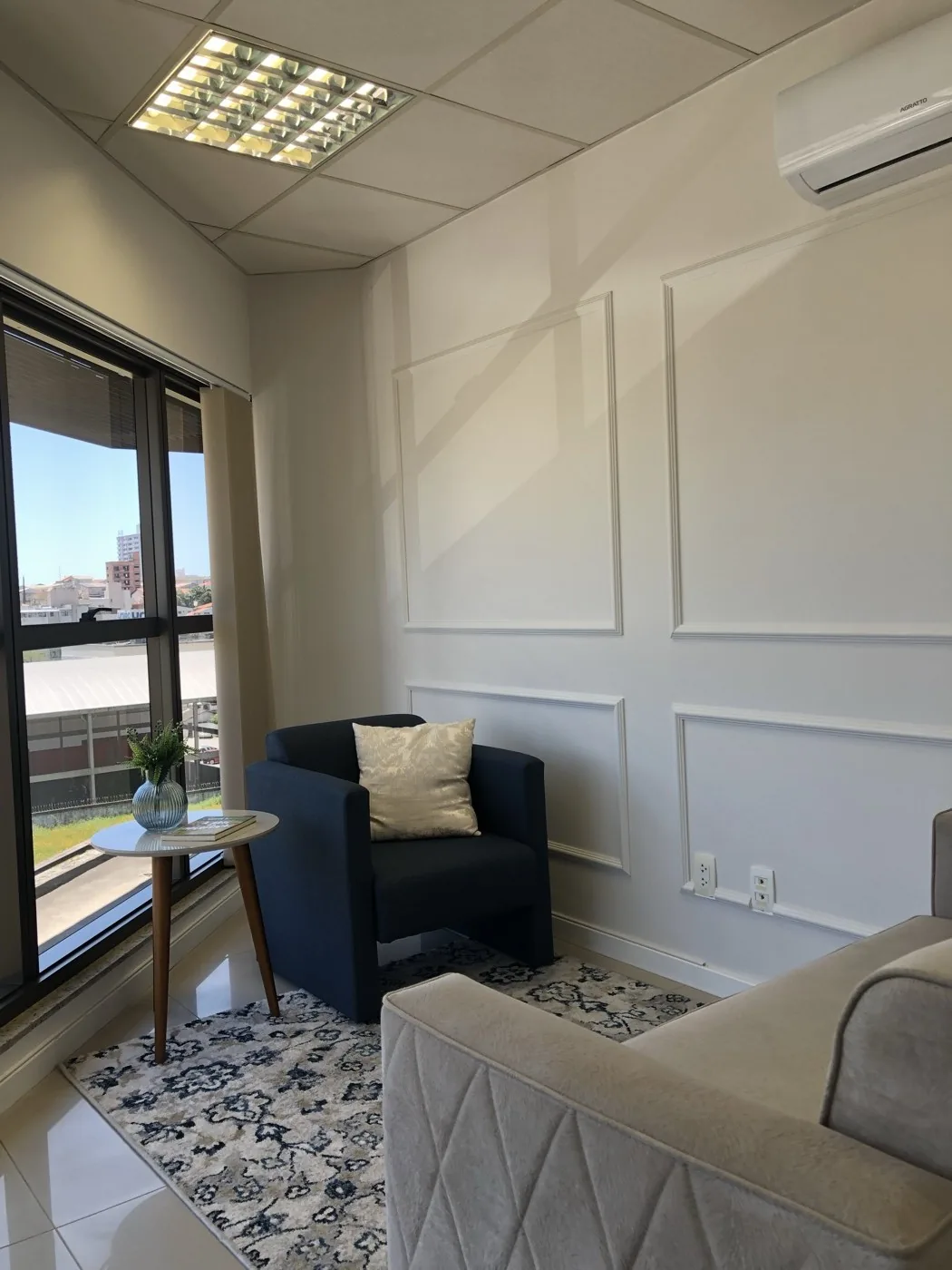 Consultório com poltrona azul, sofá e vista para a janela
