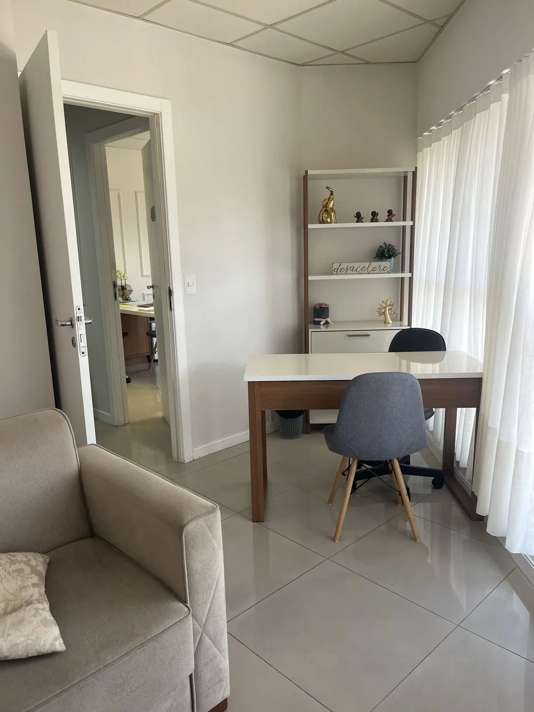Sala com mesa de atendimento, poltrona e estante decorada